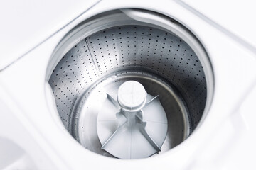 Naklejka premium Top load washing machine drum inside view. Clean empty stainless steel washer interior. Household laundry appliance closeup. Modern home equipment detail. White minimal domestic background.