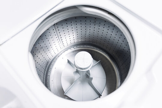 Top load washing machine drum inside view. Clean empty stainless steel washer interior. Household laundry appliance closeup. Modern home equipment detail. White minimal domestic background.