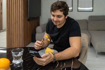 Young man eating breakfast while using smartphone at kitchen table