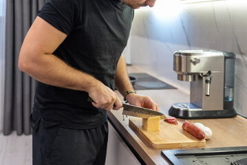 Male hands slicing hard cheese with chef knife on wooden board