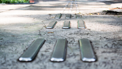Close-up of a metal tactile paving path on a concrete sidewalk, designed as directional guidance for visually impaired pedestrians.