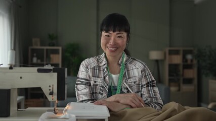 Asian female tailor smiling at her sewing machine