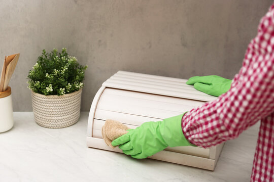 Woman wiping dust from breadbox at white marble countertop in kitchen, closeup