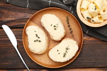 Slices of baguette with butter, thyme and knife on wooden table, flat lay