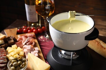 Dipping piece of bread into fondue pot (caquelon) with melted cheese at wooden table, closeup