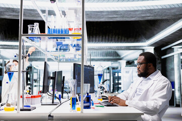 High tech lab specialist doing genetics study using clinical equipment, checking analysis results on computer. African american man using scientific gear at workbench, doing complex experiments