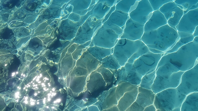 Abstract shot of clear blue water with dancing caustic sunlight patterns and soft ripples.
