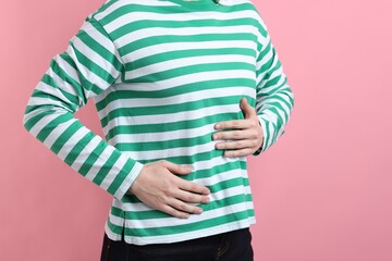 Woman suffering from stomach ache on pink background, closeup