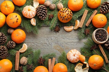 Ripe tangerines, spices, walnuts, fir tree branches and cones on wooden table, flat lay. Space for...