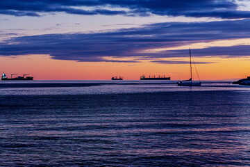 Sagome di navi da trasporto e barca a vela al tramonto viste dal lungomare di Salerno (Campania , Italia)