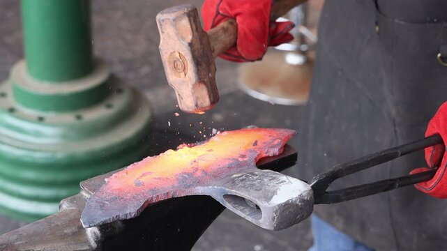 Craftsman expertly hammering heated metal on an anvil while showcasing traditional blacksmithing during axe making
