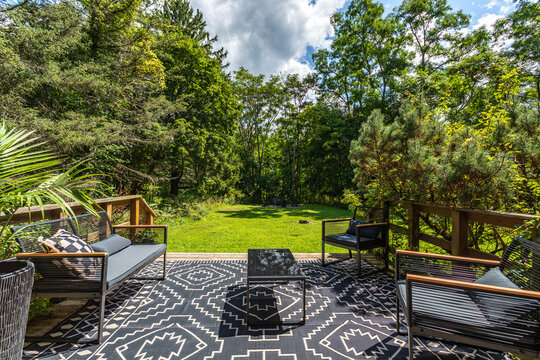 Outdoor patio lounge with modern seating and rug overlooking green backyard and forest, sunny summer deck with relaxing garden view