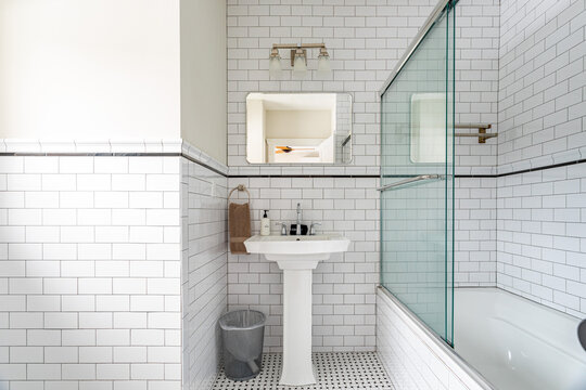 Bright white bathroom interior with subway tile walls, pedestal sink and glass shower enclosure, clean classic home design with minimal styling