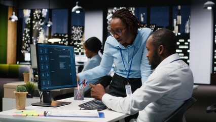 Black IT engineers team developing app and software algorithm on pc, working in the office late at night. Specialists use digital tools and focuses on script engineering and coding.