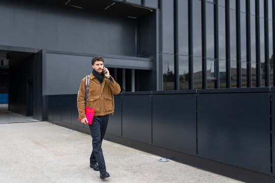 Man walking and talking on mobile phone outside modern office building in urban environment