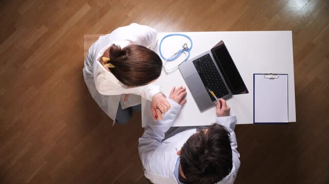 Medical team in white coats collaborating over a laptop at a desk, reviewing patient data and plansmodern healthcare consultation emphasizing teamwork, technology, and clinical expertise