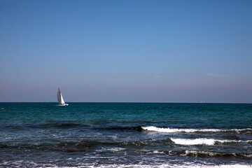 Obraz premium sailboat on the sea, Rocky Shoreline and Breakwater under Clear Blue Sky