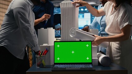 Real estate experts analyzing blueprints and models next to green screen, working on new urban development project through planning phases and infrastructure design. Urban growth.