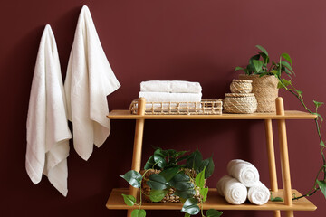 Shelf unit with clean towels and plants near burgundy wall in room