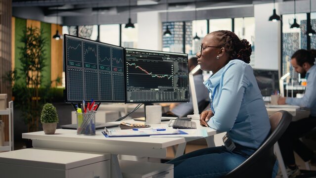 Portfolio manager in brokerage company office analyzes stock market trends to increase returns. African american woman tracks stock exchange metrics to identify investment opportunities
