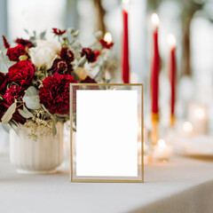 Romantic table setup with blank table sign in gold frame, glowing candles, and rich red florals