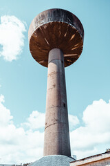 Low angle wide view of a tall concrete water tower with mushroom head against blue sky and clouds, brutalist industrial architecture landmark, minimal background