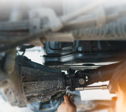 A skilled mechanic tightens the nuts on the differential driveshaft universal joint using a wrench. This is part of routine maintenance and repair, including replacement of damaged or worn parts.