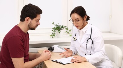 Doctor with clipboard consulting patient at wooden table in clinic