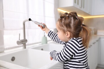Child safety at home. Little girl pulling down faucet hose at sink in kitchen
