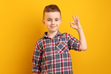 Happy boy showing okay gesture against yellow background
