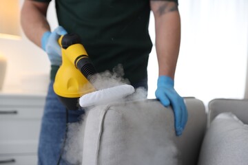 Pest control worker cleaning sofa with steam cleaner indoors, closeup