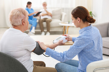 Obraz premium Caregiver measuring senior woman's blood pressure at home
