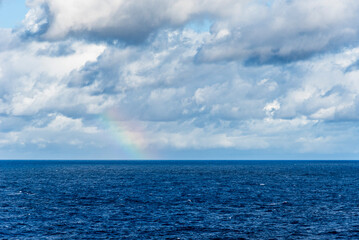 Calm ocean under cloudy sky with rainbow on the horizon, concept of hope, balance and renewal after uncertainty, minimal seascape background.