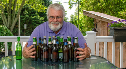 A man with a beard sits at a table surrounded by various empty and one full beer bottle. He appears joyful, displaying a sense of accomplishment and relaxation on a sunny day.