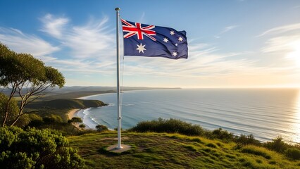 Fototapeta premium Australian flag waving on a hill overlooking a serene coastal landscape with green grass and trees under a partly cloudy blue sky at sunrise