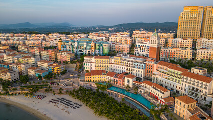 Obraz premium Aerial view of Sunset Town on Phu Quoc Island, Vietnam, showcasing pastel-colored European-style buildings, beach, and palm trees under clear blue sky.