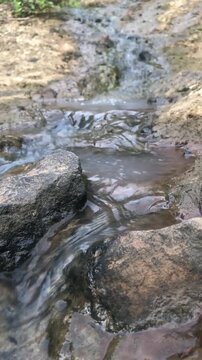 Shallow stream gliding over stones with soft natural reflections. Clear trickle between rocks in quiet woodland setting. Small creek flow across rugged surface for zen background.