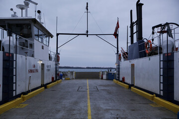 Symmetrical view from an empty vehicle ferry deck looking toward open water under an overcast sky,...