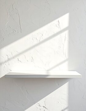 Bright sunlight casts shadows across a textured white wall with a single, simple shelf
