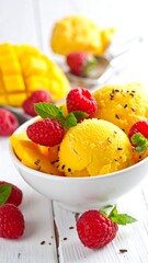 Bright yellow mango ice cream in a bowl, topped with raspberries and mint sprigs on a rustic white wooden surface