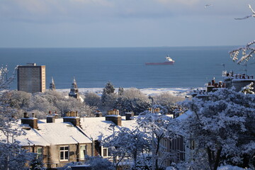 Snow Covered Coastal Town Overlooking Calm Sea With Distant Ship On Horizon Winter Morning View