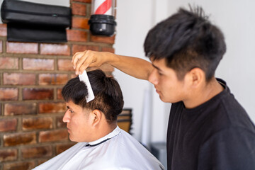 Latino barber combing client's hair in shop