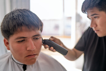 Barber cutting young man's hair using electric trimmer