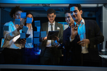 Obraz premium Corporate marketing team planning business growth strategy. Executives analyzing financial goals and market trends using sticky notes on glass wall in modern office.