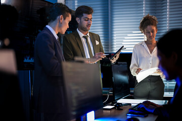 Automotive executives discussing electric car market strategy. Business leadership team analyzing vehicle sales data and future design trends in modern night office.