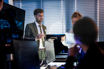 Autonomous driving software team reviewing car AI simulation. Engineers and managers discussing self-driving vehicle safety systems in high-tech control room center.
