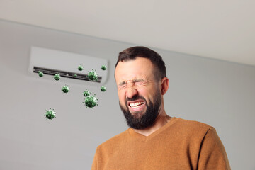 Man grimacing because of bad smell from air conditioner indoors, low angle view. Bacteria flying from appliance