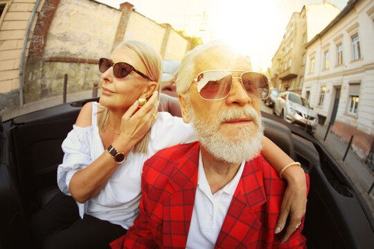 Stylish elderly couple enjoying ride in convertible car, wide angle lens