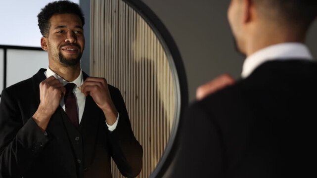 Handsome man adjusting tie near mirror at home