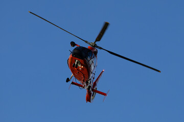 Red helicopter in flight against clear blue sky with spinning rotor blades — dynamic aviation image capturing rotary-wing motion, aerodynamic design, and airborne perspective from below © Good Design #8